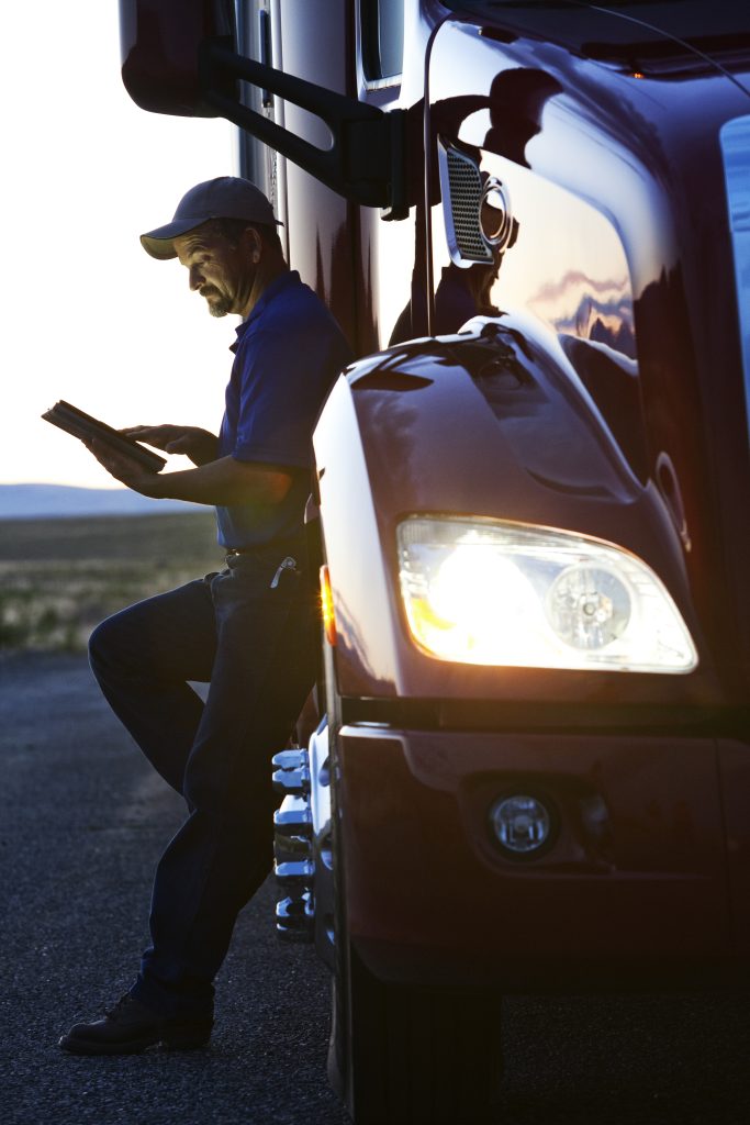 a person sitting on the side of a semi truck holding a tablet